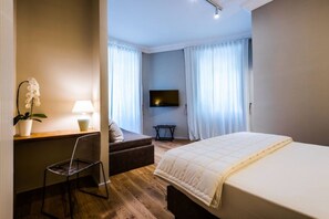 A modern hotel room with a large bed, a desk with a chair, a TV, and a potted plant. - Giselda Home (Rome)