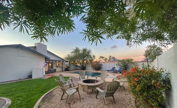 A backyard with a fire pit, outdoor seating, a swimming pool, and a well-maintained lawn.