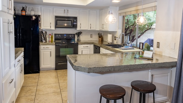 A modern kitchen with white cabinetry, a central island with stools, a built-in oven, and a microwave. - Spacious Yard, Pool, Pet & Kid Friendly, Close to Everything! (Mesa)
