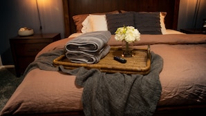A neatly made bed with a brown headboard, a tray with folded towels, a remote control, and a vase with flowers. - Spacious Yard, Pool, Pet & Kid Friendly, Close to Everything! (Mesa)