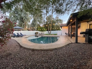A backyard with a swimming pool, lounge chairs, and a barbecue area.