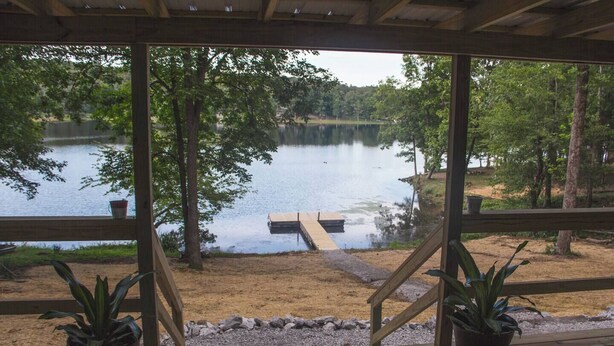 Una terraza techada con vistas a un lago, deck de madera y plantas en macetas.