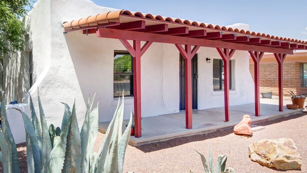 Een gebouw met een witte gevel, een rode houten pergola en cactussen op de voorgrond.