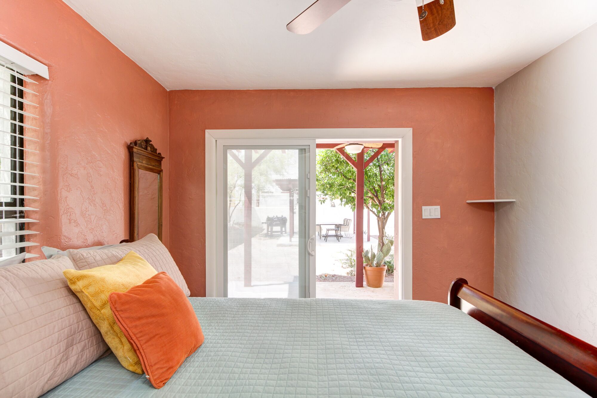 A bedroom with a bed, a window with blinds, a door leading to an outdoor area, and a ceiling fan.