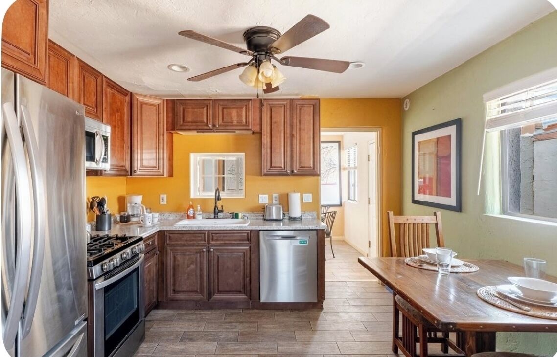 A kitchen with wooden cabinets, stainless steel appliances, a central island, and a dining area with a table and chairs.