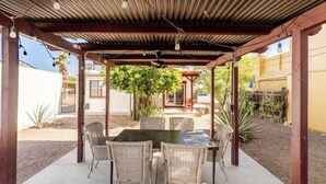 Een overdekt terras met een tafel, stoelen, een plafondventilator en lichtslingers.
