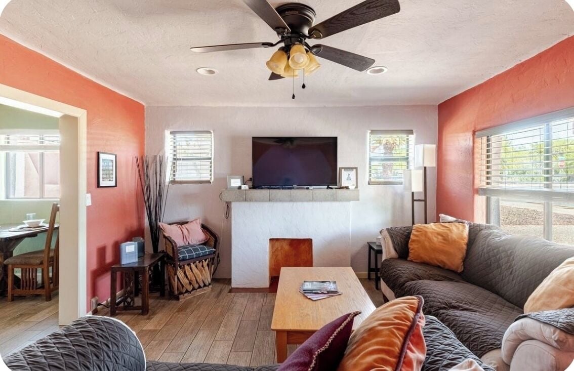 Uma sala de estar com ventilador de teto, lareira, televisão e um sofá.
