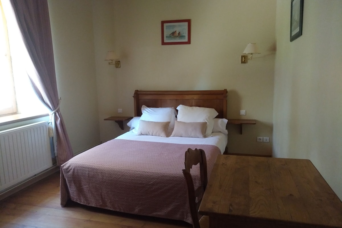 Una habitación con una cama, una mesa de madera y dos lámparas fijadas a la pared.