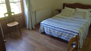 Een slaapkamer met een bed, een stoel, een radiator, een nachtkastje en een raam met gordijnen.