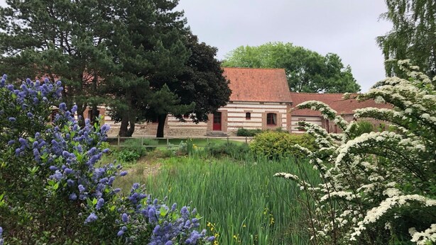 Een klassiek bakstenen gebouw met een rode dakbedekking, omgeven door weelderige begroeiing en bloeiende planten.