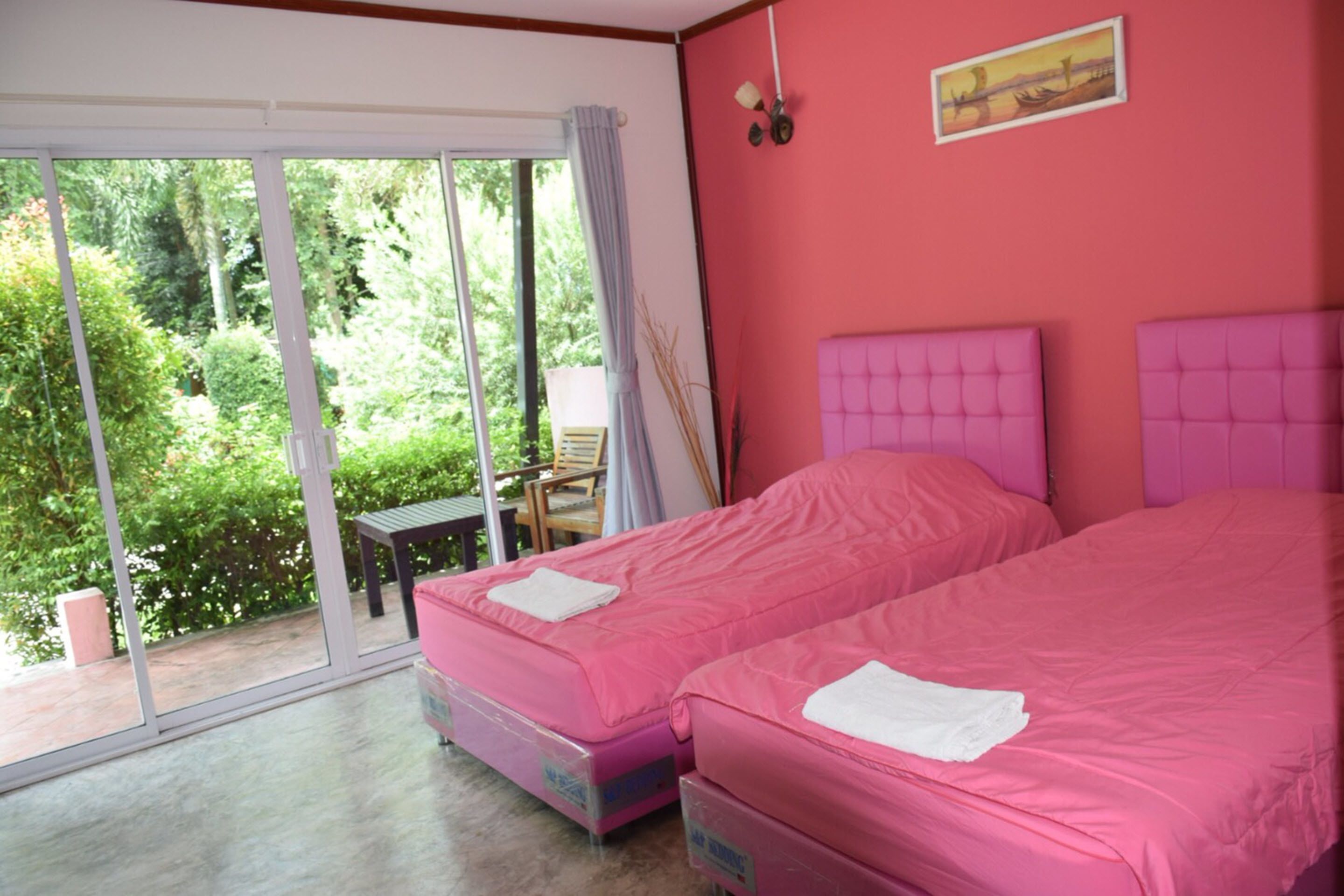 A room with two pink beds, a sliding glass door to a balcony, a small table, and a chair.
