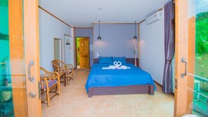 A bedroom with a bed, two chairs, a wooden door, and a view of greenery.