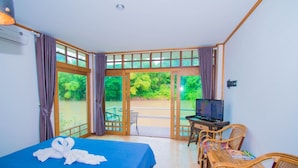 A room with a bed, a desk with a computer, and a view of greenery outside.