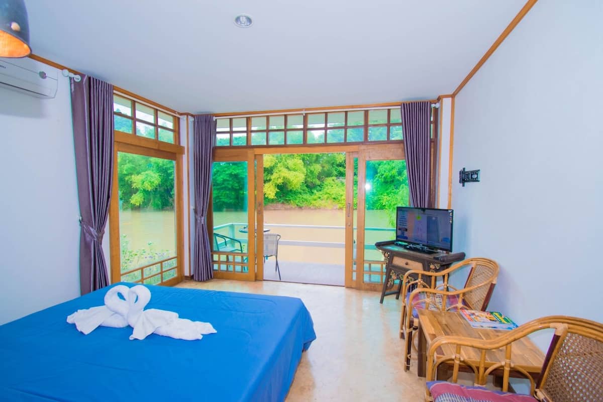 A room with a bed, a desk with a computer, and a view of greenery outside.