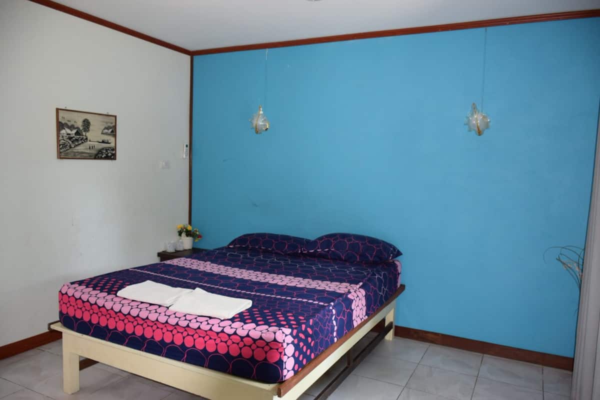 A bedroom with a bed, a nightstand, a wall-mounted lamp, and a framed picture.