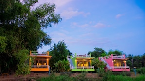 Three colorful floating houses with balconies, situated on a calm body of water surrounded by greenery.