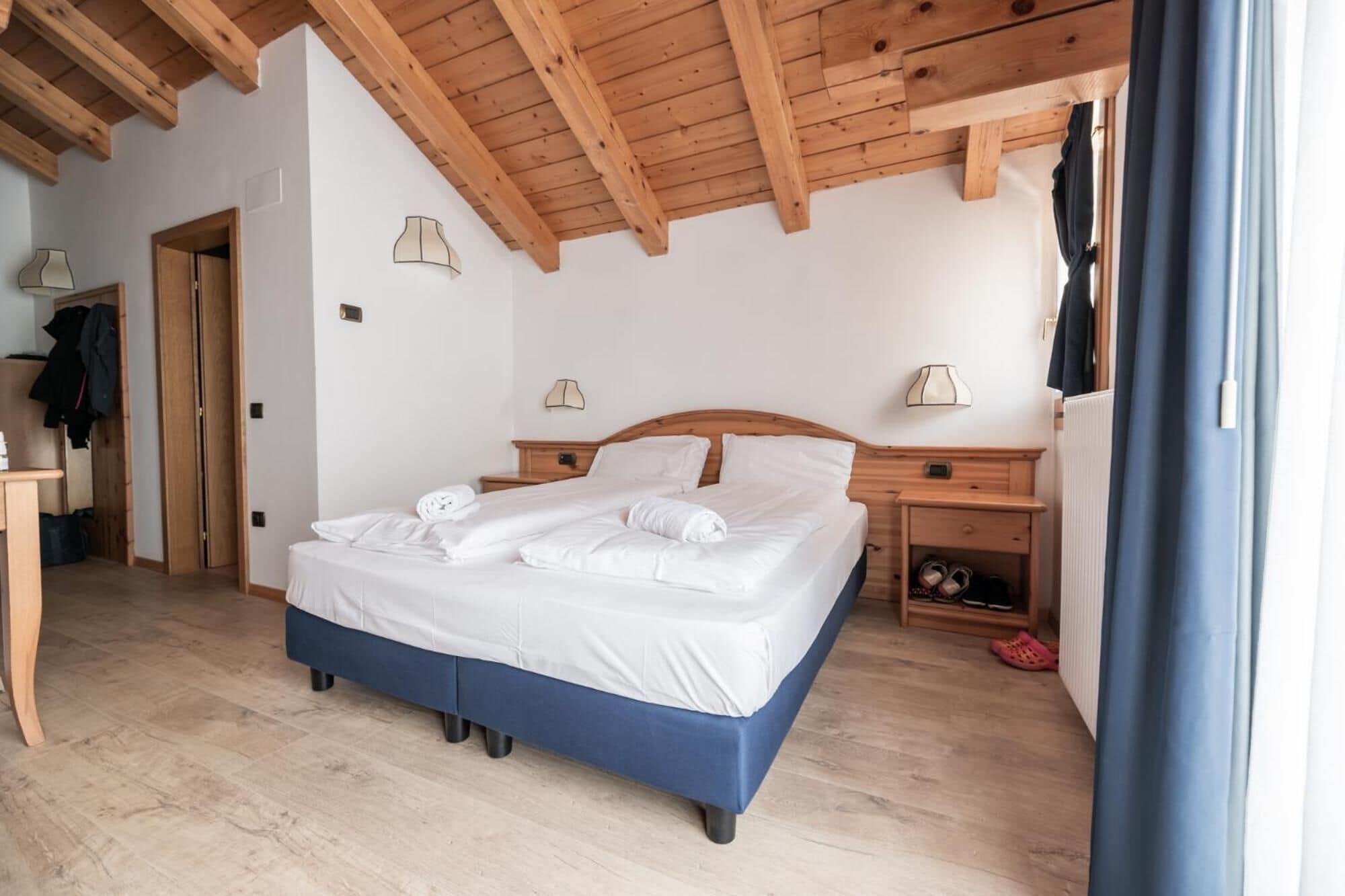 A bedroom with a wooden ceiling, a bed with white bedding, two bedside tables with lamps, and a wooden floor.