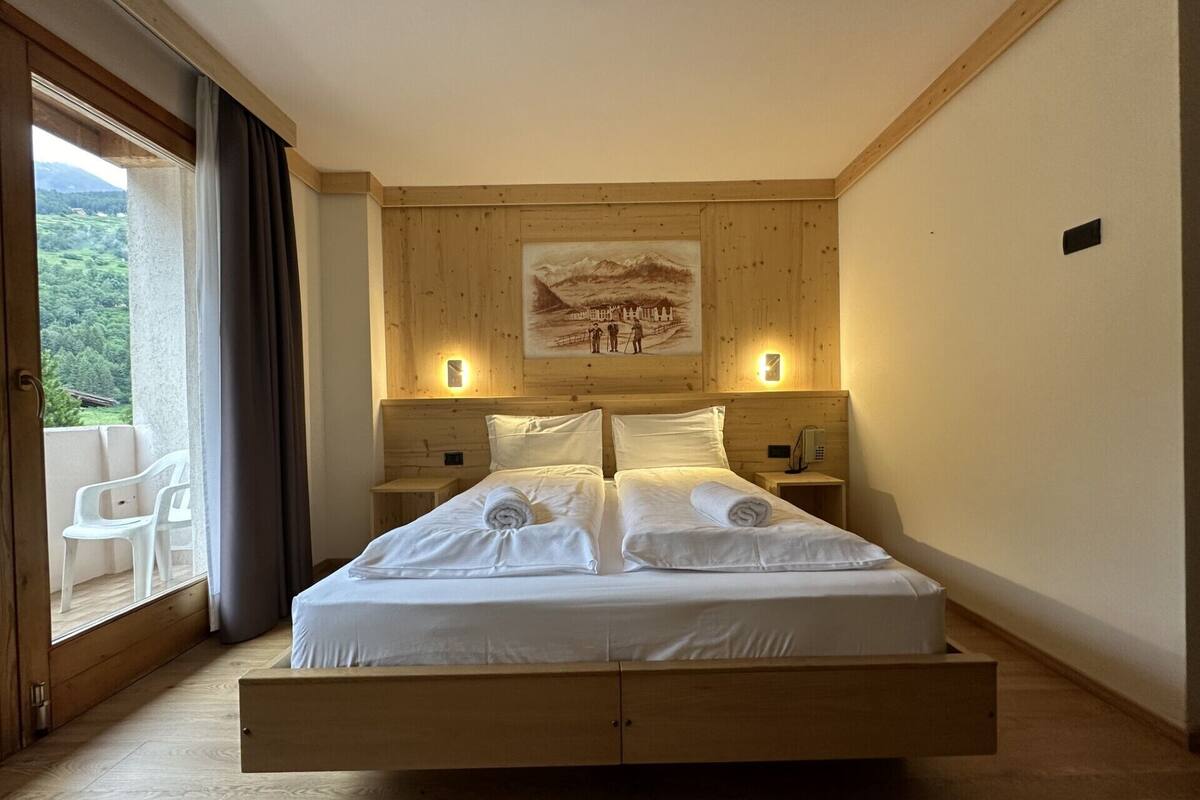 A bedroom with a wooden headboard, a bed with white linens, two bedside tables with lamps, and a painting on the wall.
