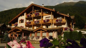 A multi-story hotel with balconies adorned with flower boxes, set against a mountainous backdrop. - Hotel Gran Zebrù (Pejo)