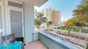 A balcony with a table and chairs, a view of a street and buildings, and a clear sky. - Houghton Place Sea Point (Cape Town)