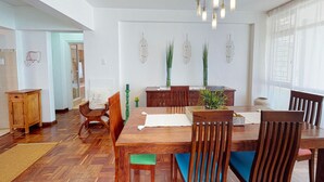 A dining area with a wooden table, chairs, and a chandelier. There are decorative wall art pieces and a potted plant on the table. - Houghton Place Sea Point (Cape Town)