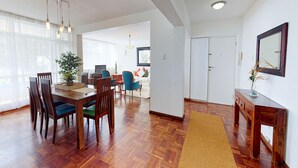 A spacious living area with a wooden dining table, chairs, and a large window. - Houghton Place Sea Point (Cape Town)