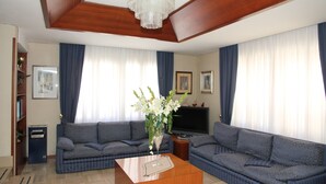 A living room with two blue sofas, a wooden coffee table, a TV, and a chandelier. - Hotel Da Remo (Roccaraso)