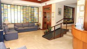 A spacious lobby with a wooden staircase, a sofa, and a reception desk. - Hotel Da Remo (Roccaraso)