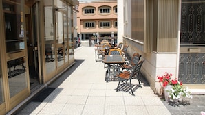 An outdoor café with tables and chairs, a building entrance, and a flower pot with red flowers. - Hotel Da Remo (Roccaraso)