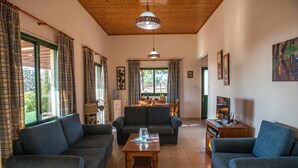 A living room with two sofas, a coffee table, a TV, and a dining area in the background. - Adonis Villa (Pegeia)