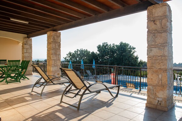 A covered outdoor area with stone pillars, lounge chairs, and a pool. - Adonis Villa (Pegeia)