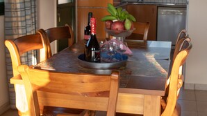 A dining area with a wooden table and chairs, a fruit bowl, and a bottle of wine. - Adonis Villa (Pegeia)