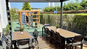 An outdoor patio area with a covered seating arrangement, a play structure, and a view of the surrounding greenery.