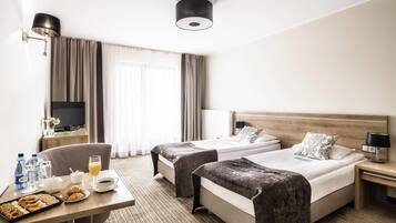 A hotel room with two beds, a TV, a desk with breakfast, and a large window with curtains.