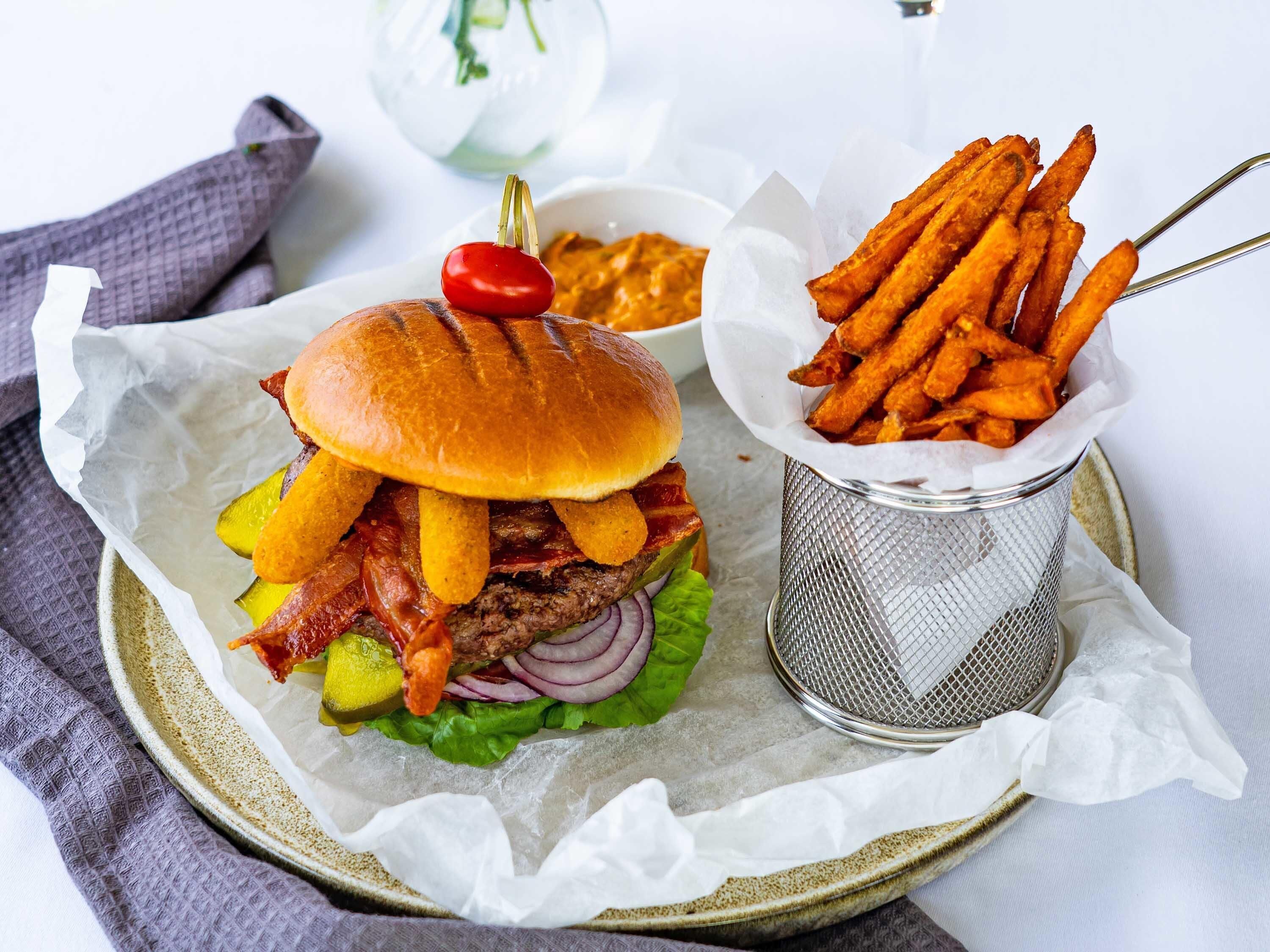 A burger with fries and a small bowl of sauce on a plate.