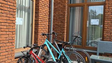 Edifício de tijolos com duas bicicletas estacionadas na frente, um banco e uma janela com vista para árvores.