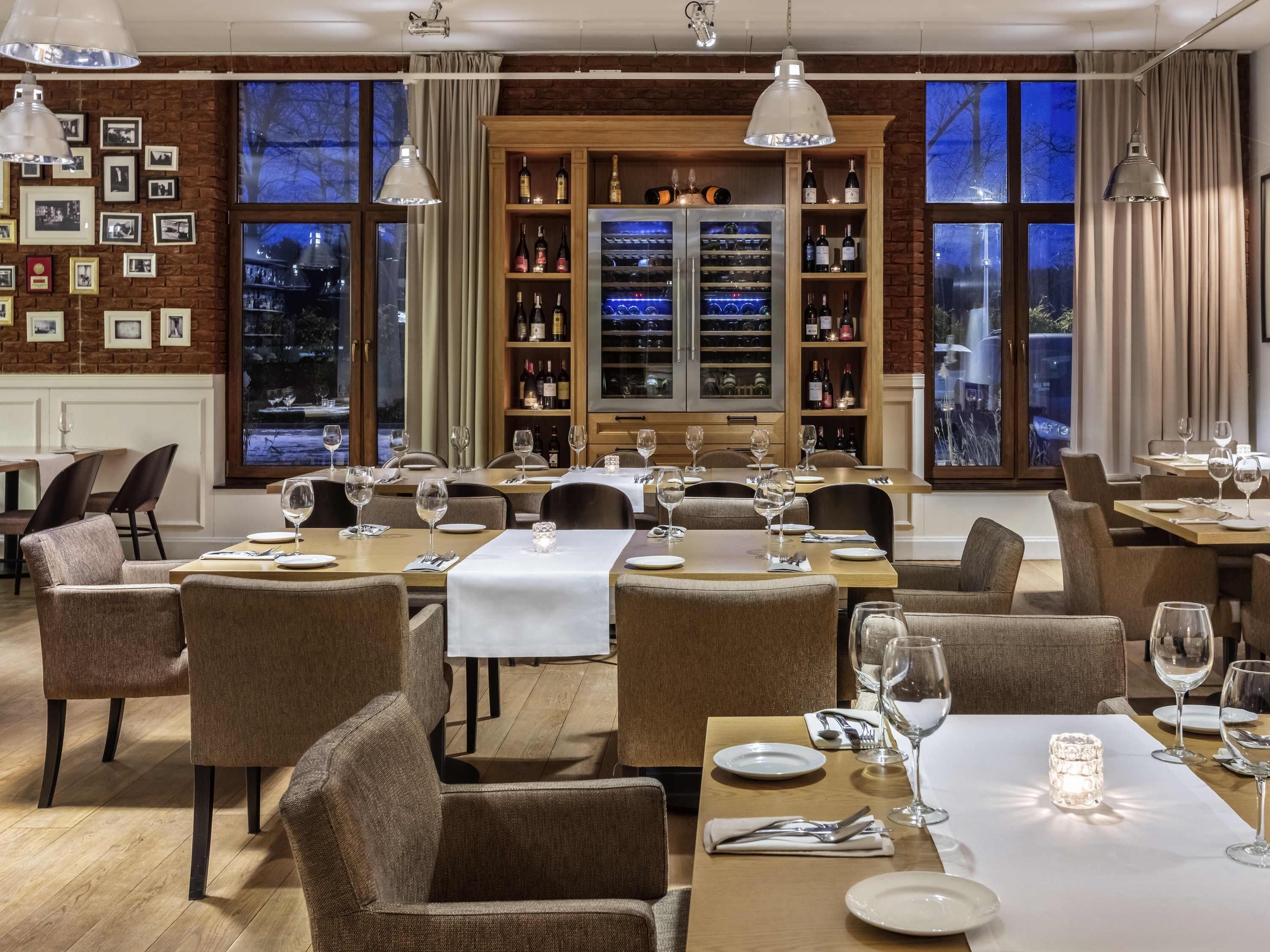 Un restaurante con mesas dispuestas para comer, una exhibición de vinos y cuadros en la pared.