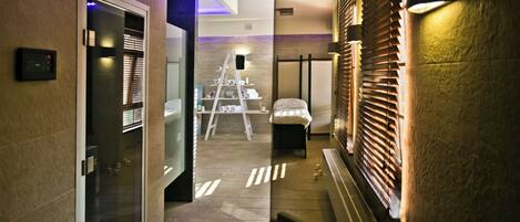 A hotel corridor with a glass door, a ladder, and a bed in the background.
