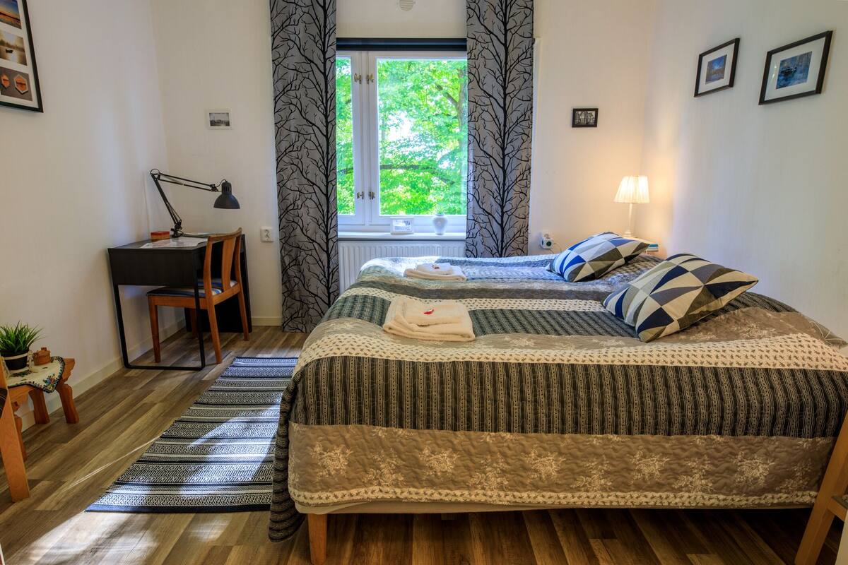 Ein Schlafzimmer mit Bett, Schreibtisch, Stuhl, einem Fenster mit Vorhängen und einer Lampe.