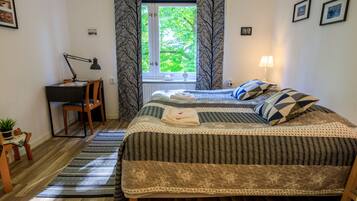 A bedroom with a bed, a desk, a chair, a window with curtains, and a lamp.