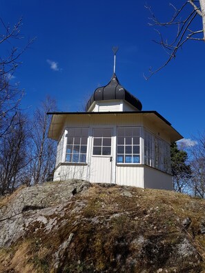 A small, white, two-story building with a pointed roof, situated on a rocky hill with sparse vegetation. - Brukshotellet Skinnsberg (Skinnskatteberg)