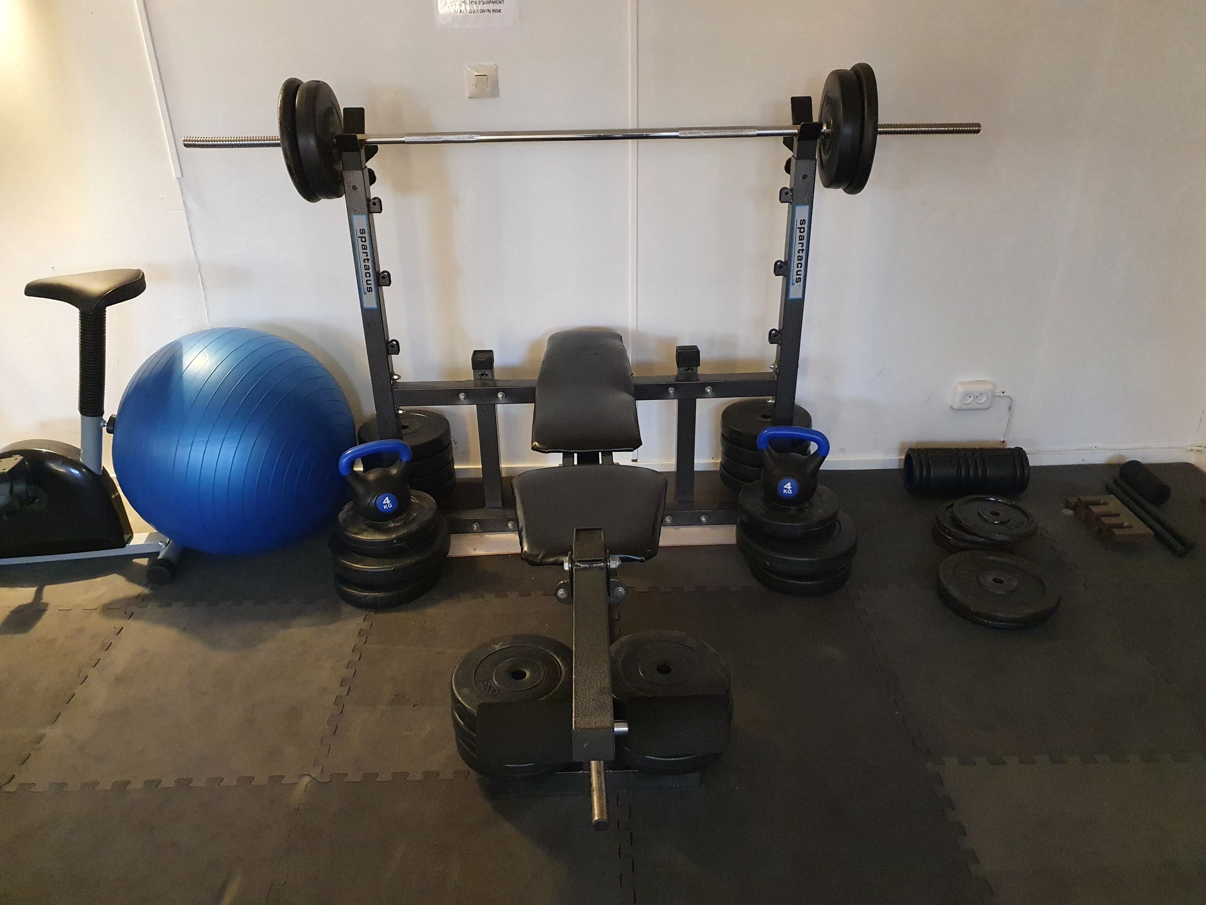A home gym with a squat rack, kettlebells, a bench, and a large exercise ball.