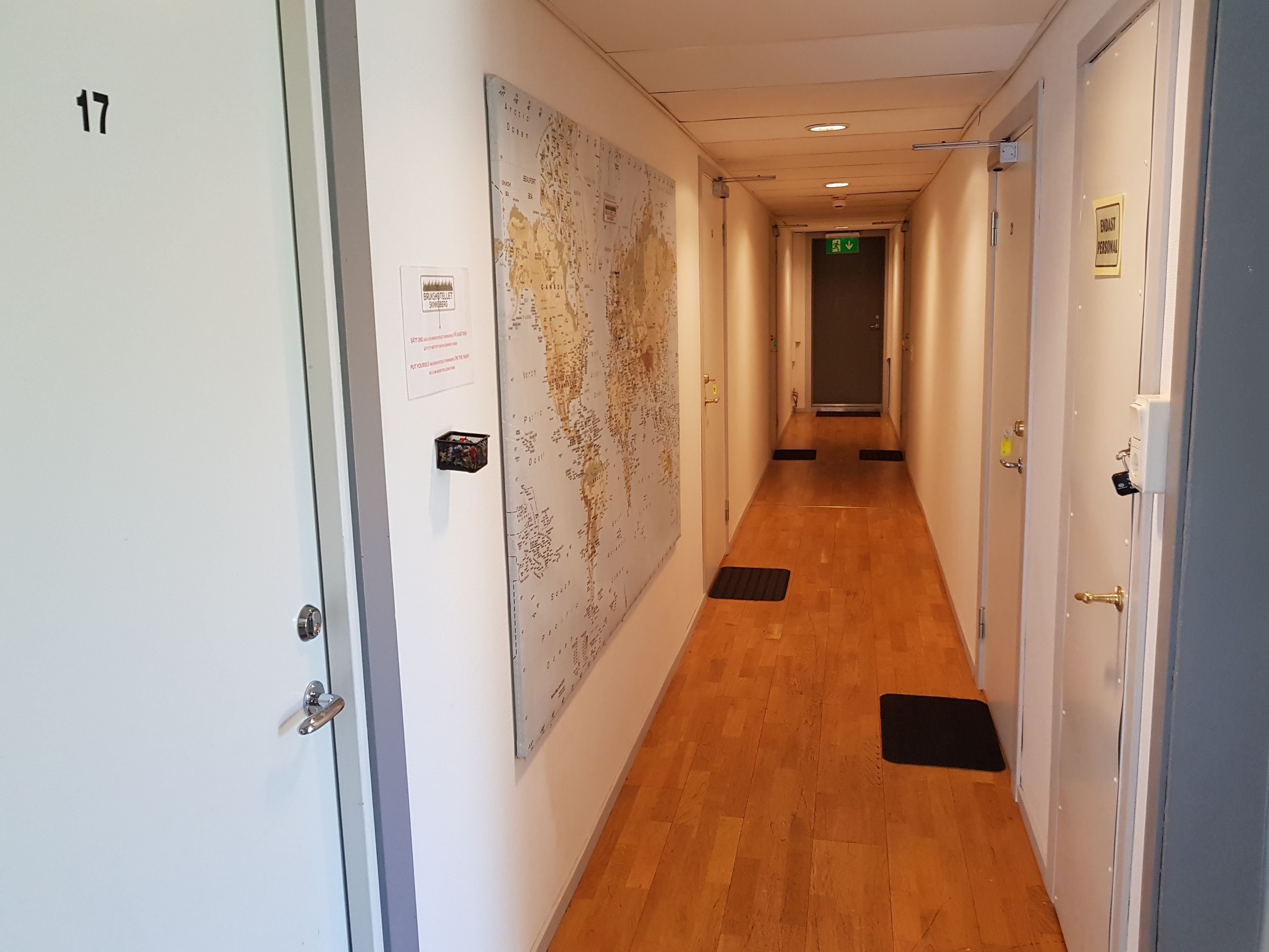 Un pasillo con piso de madera, un mapa en la pared y una puerta con la leyenda '17'.