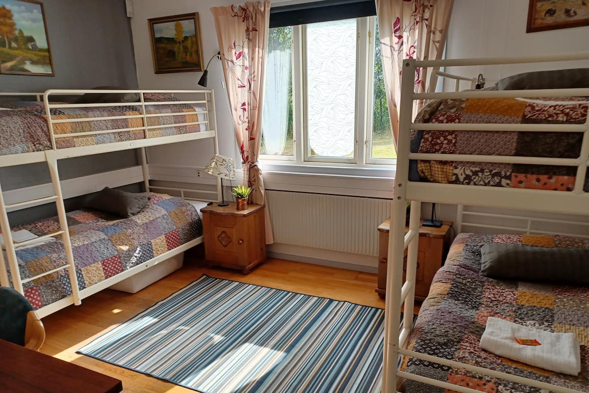 Ein gemütliches Zimmer mit Etagenbetten, einem kleinen Nachttisch mit Lampe und Pflanze, einem Streifen-Teppich und einem Fenster mit Vorhängen.