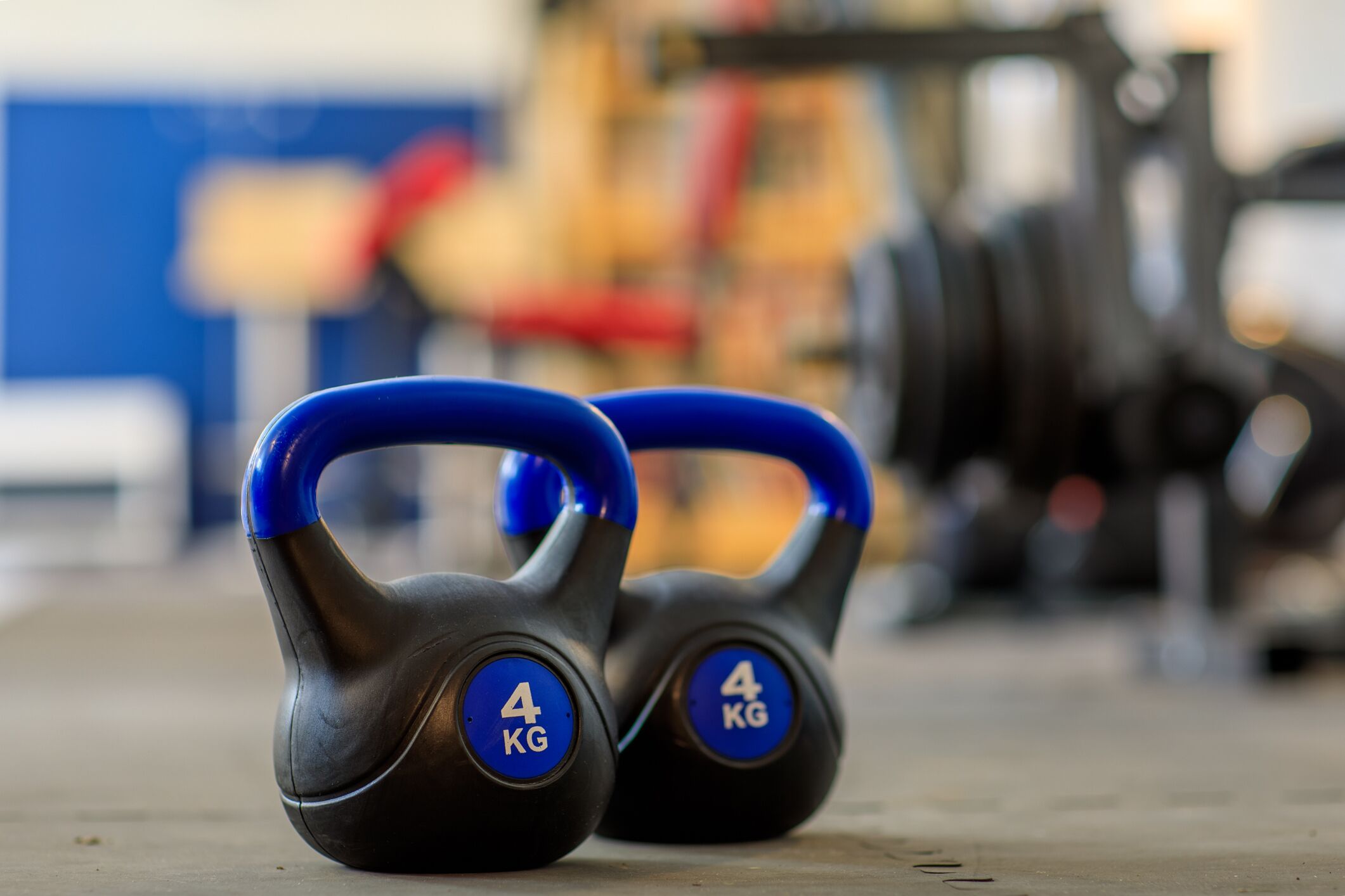 A pair of 4 kg kettlebells with blue handles on a concrete floor.