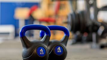A pair of 4 kg kettlebells with blue handles on a concrete floor.