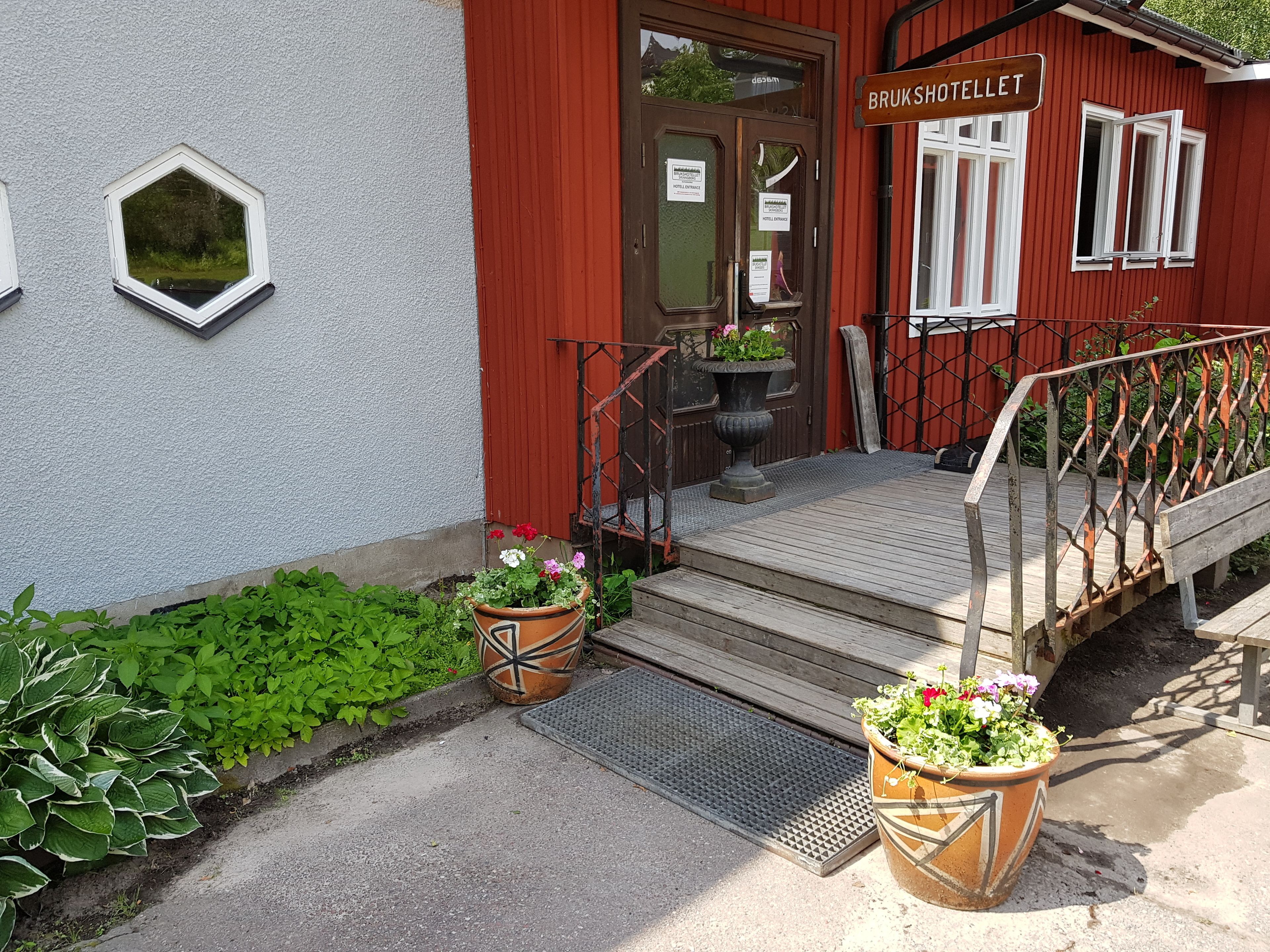 En hotellentrén med en röd fasad, en trätrappa och två blomkrukor placerade på trappstegen.