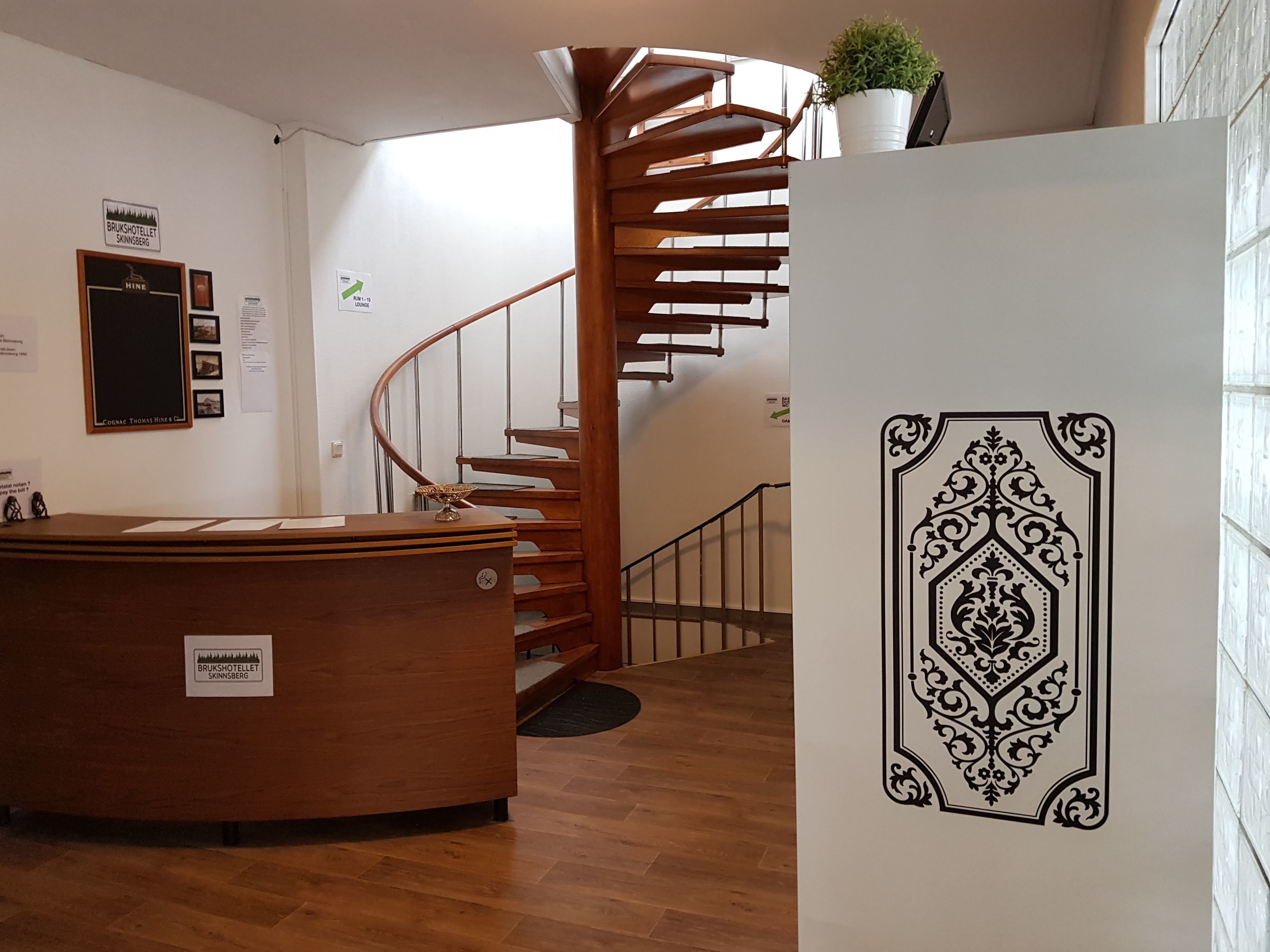 Un espace d’accueil d’hôtel avec un comptoir en bois, un escalier en colimaçon et un élément décoratif mural.