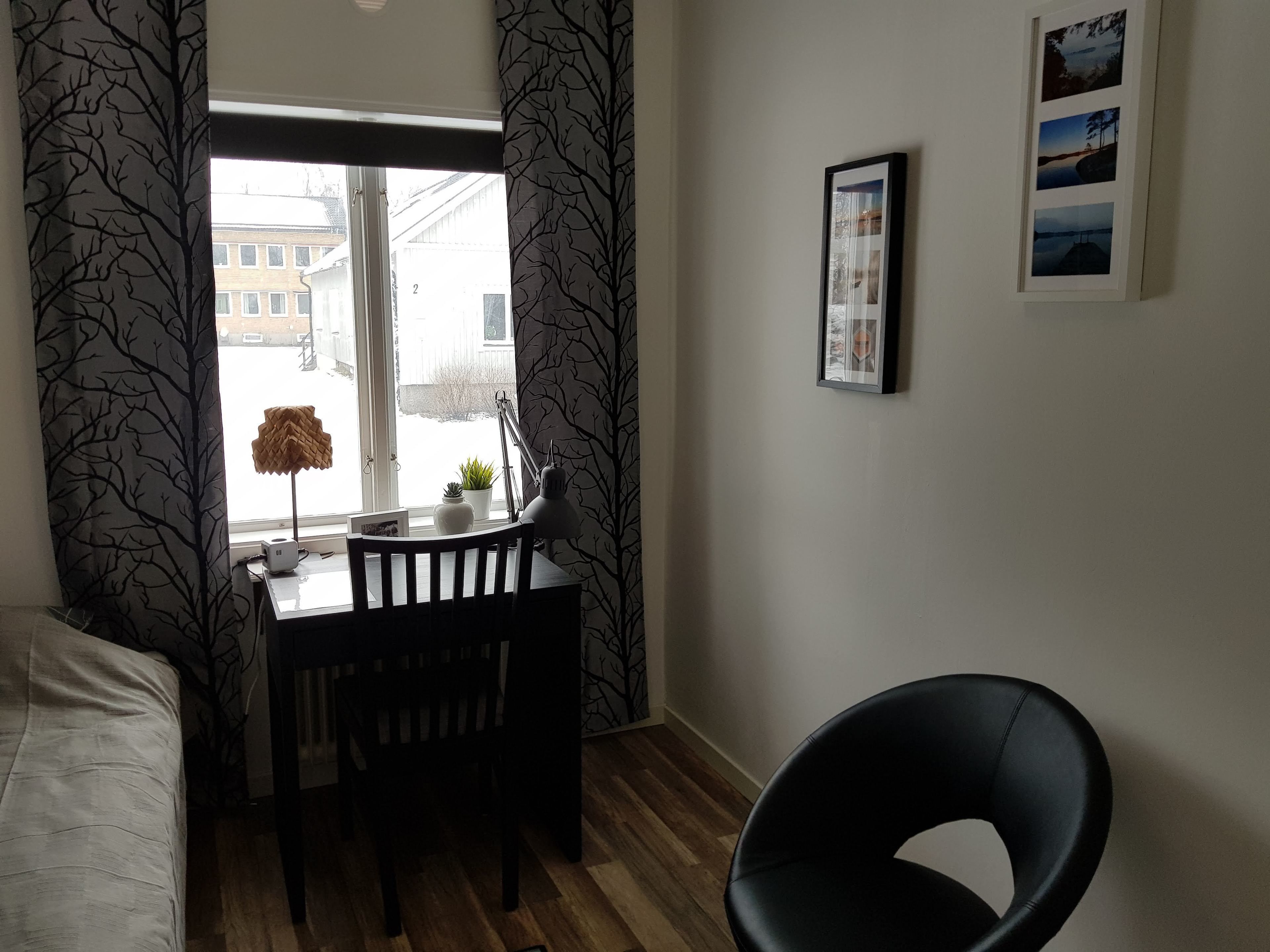 A room with a wooden desk, a chair, a bed, and a window with curtains.