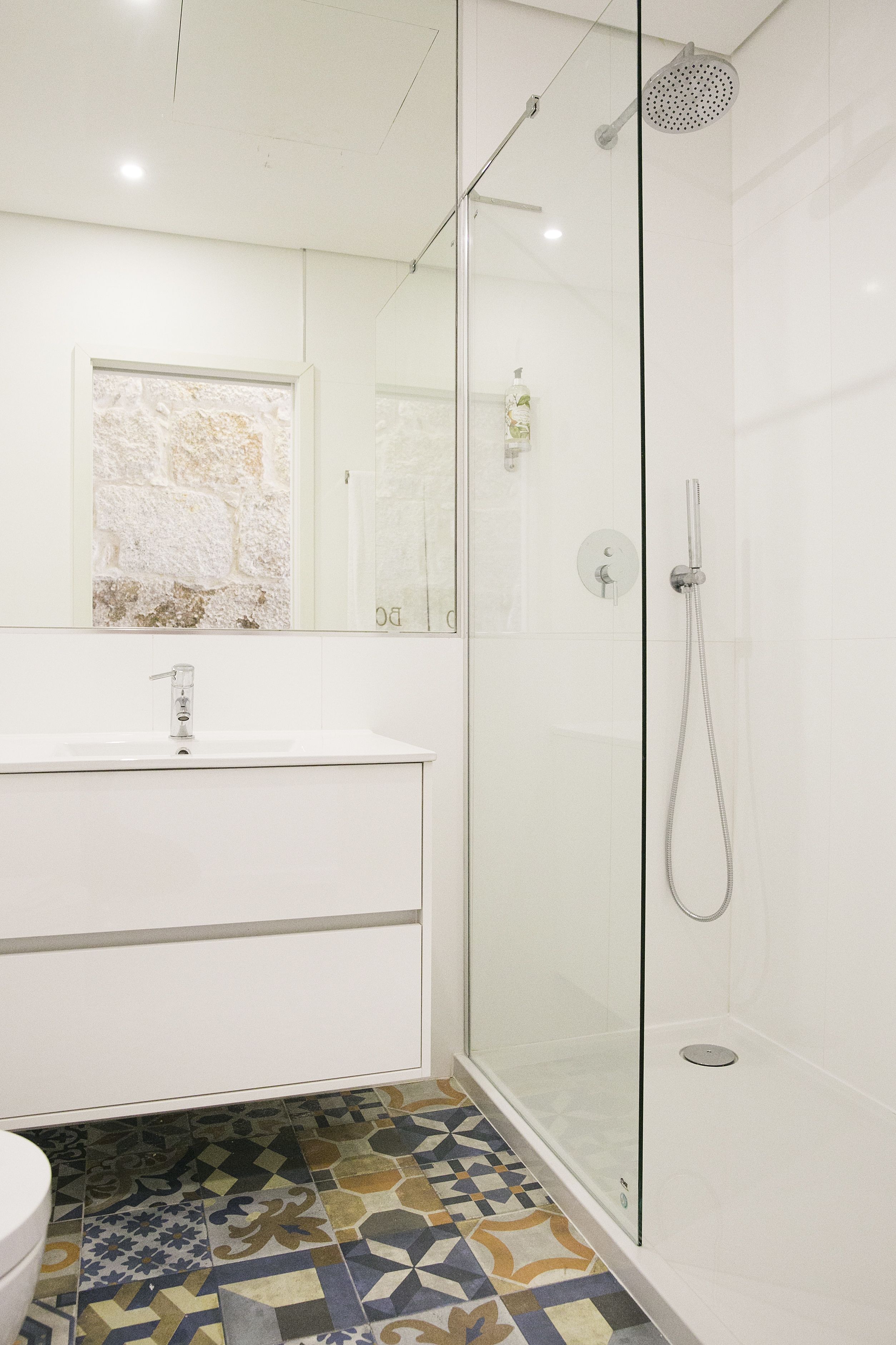 Un baño moderno con ducha de vidrio, lavamanos blanco y piso estampado.